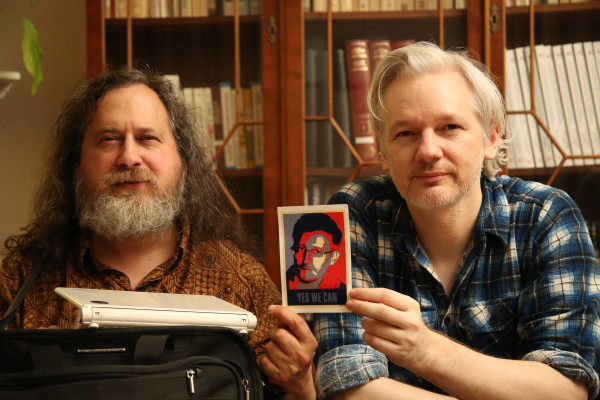 Photo of Richard Stallman and Julian Assange at the Ecuadorian embassy in London holding up a posterized, Shepard Fairey "Obey" like photo of Edward Snowden with the text "Yes we can"